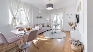 A modern living room with a sofa, dining table, and chairs. There is a round rug, a hanging light fixture, and a small side table with decorative items.