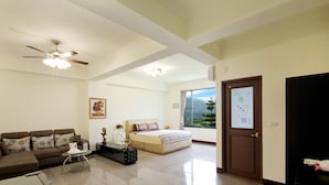 A spacious living room with a sofa, a coffee table, a ceiling fan, and a large window offering a view of greenery. - Jing Guan Yuan (Zhushan)