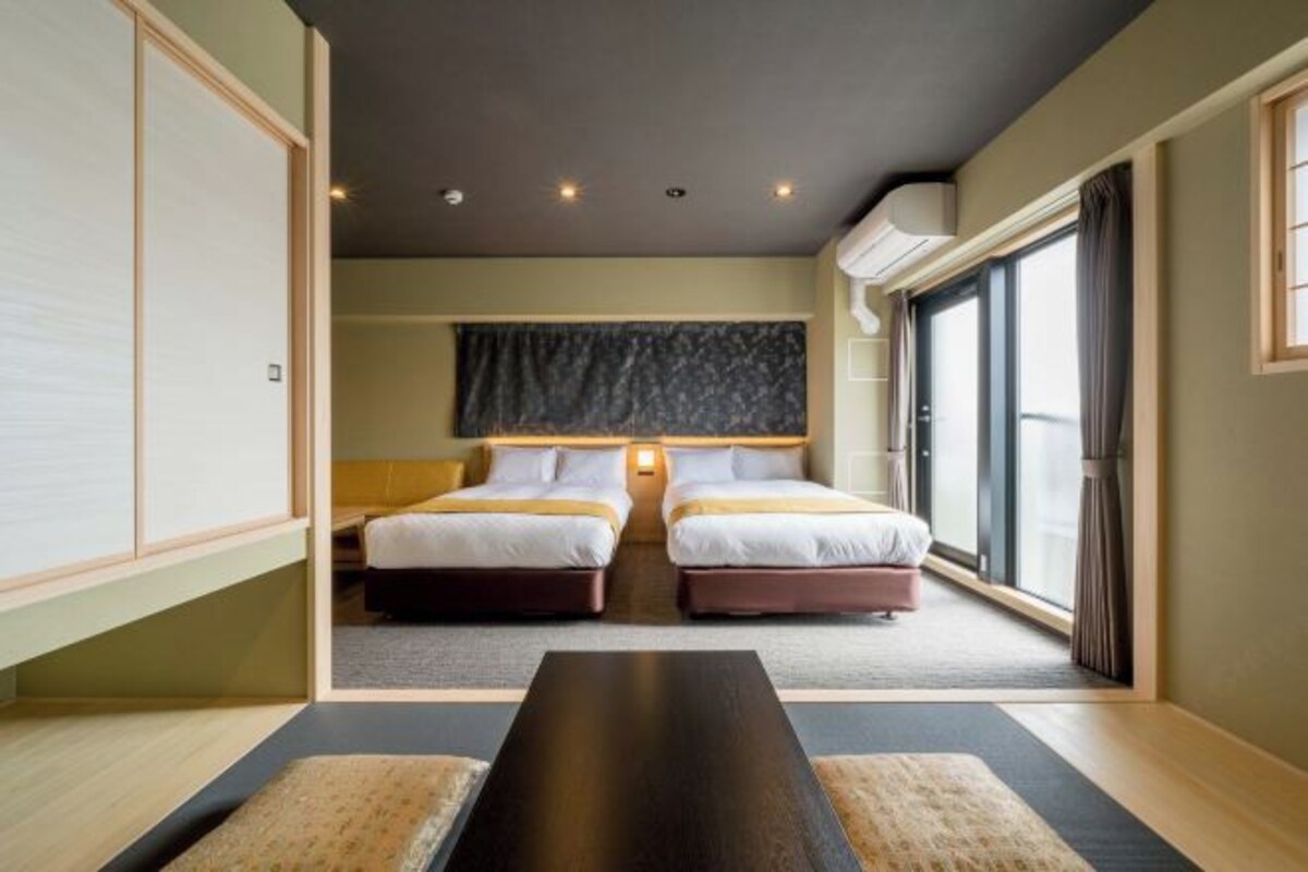 A hotel room with two beds, a large window, and a view of the outside.