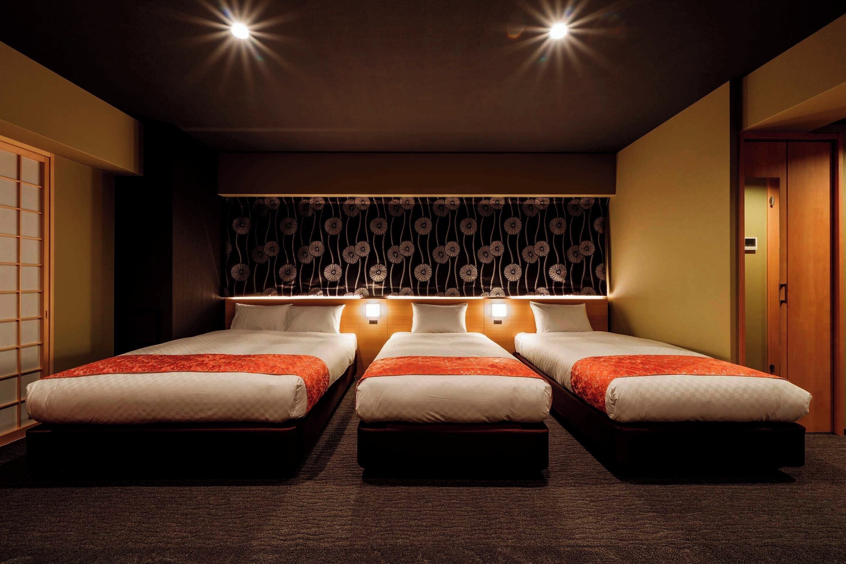 Ein Hotelzimmer mit drei Betten, einem dunklen, gemusterten Kopfteil und einer traditionellen Schiebetür.
