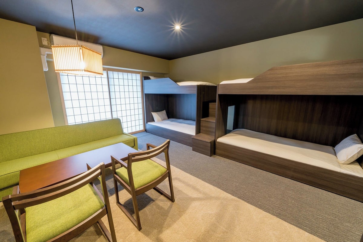 Um quarto com beliches, um sofá verde, uma mesa de madeira e cadeiras.