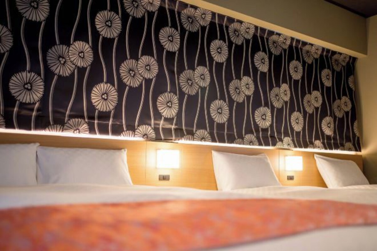 A hotel room with a bed, two bedside tables, and a wall with a floral pattern.