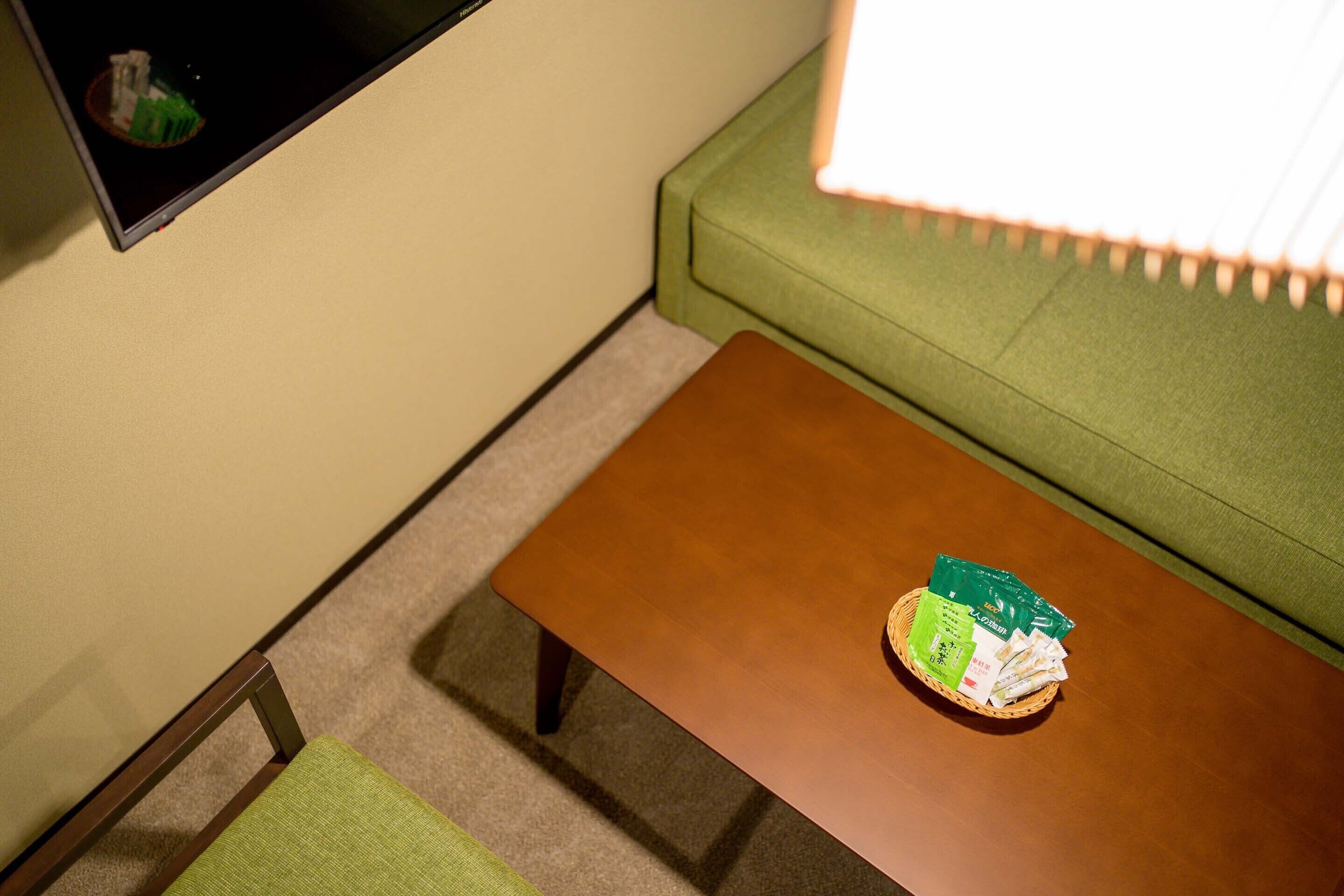 A room with a green sofa, a brown coffee table with a basket of green and white items, and a small chair.