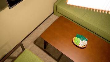 A room with a green sofa, a brown coffee table with a basket of green and white items, and a small chair.