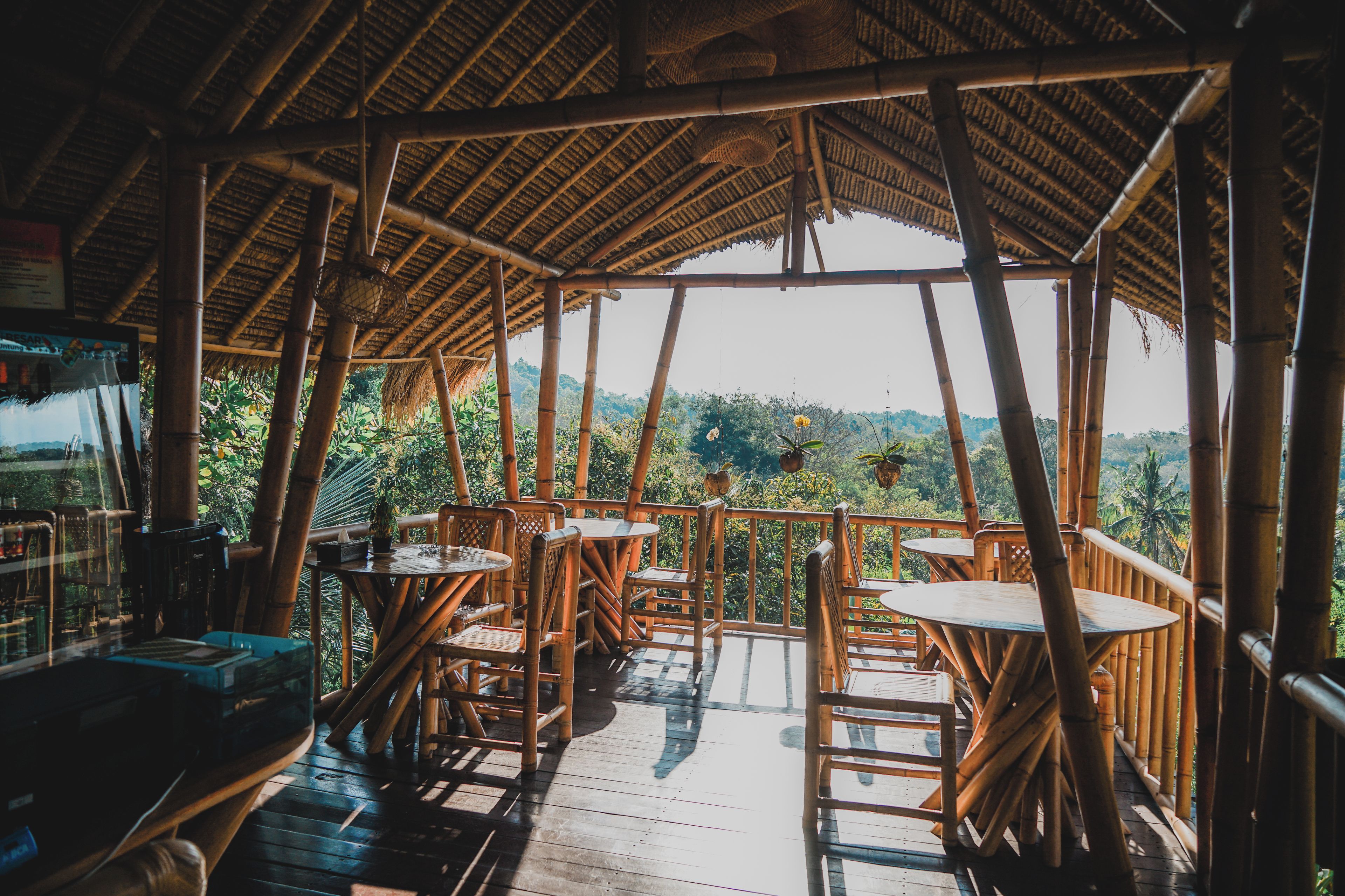 A bamboo-framed outdoor seating area with tables and chairs, overlooking a lush landscape.