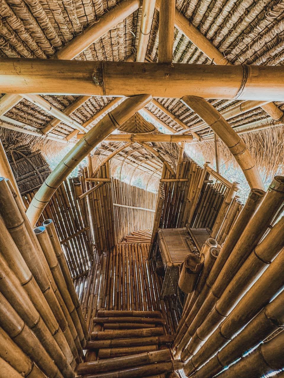 A bamboo structure with a thatched roof, a central staircase, and a view of the surrounding area.