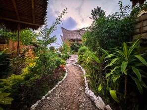 A garden pathway leading to a traditional thatched-roof structure surrounded by lush greenery. - Penida Bambu Green Villas (Penida Island)