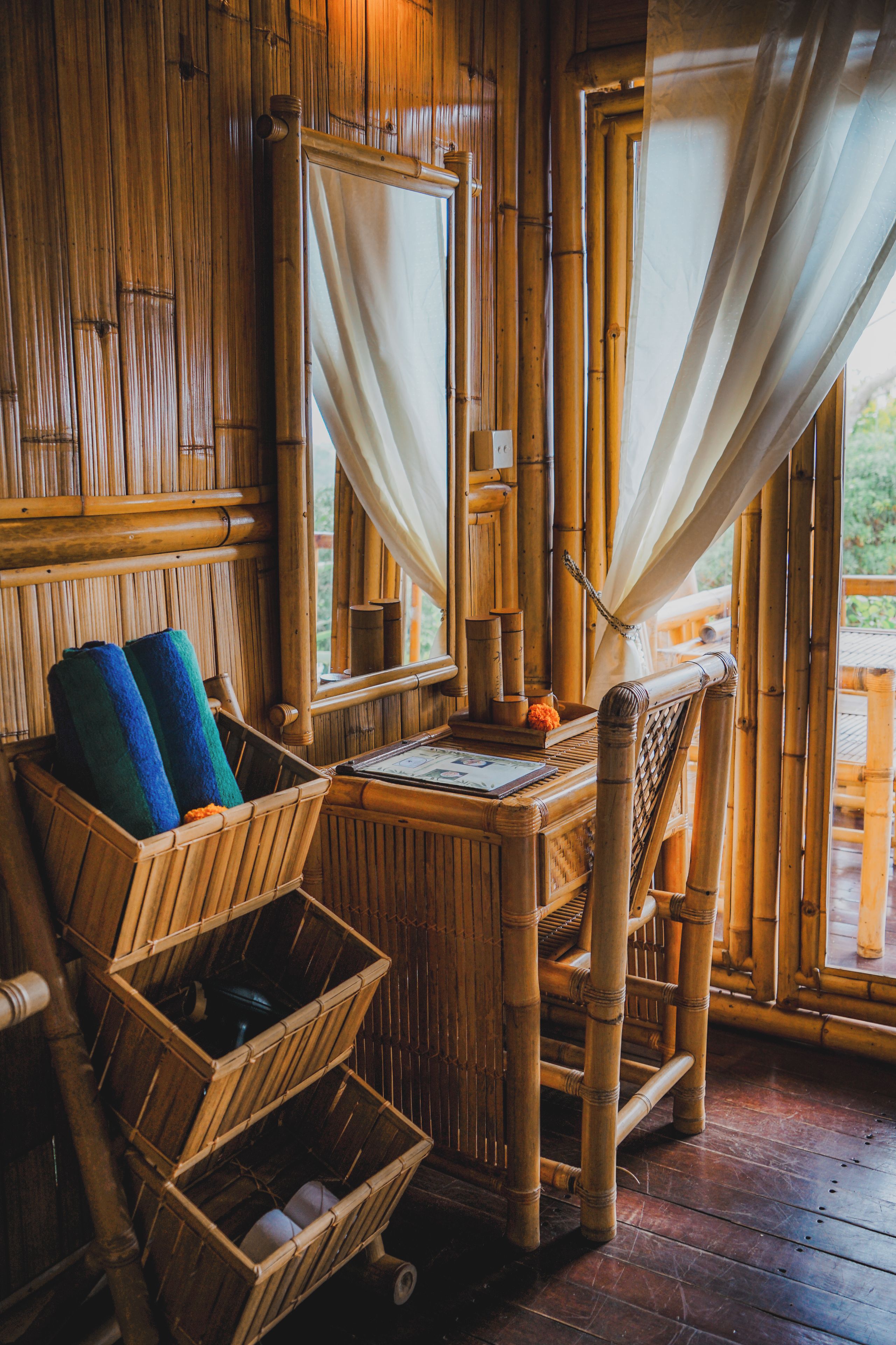A bamboo-framed room with a bed, a small table, and a window with curtains.