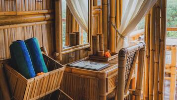 A bamboo-framed room with a bed, a small table, and a window with curtains.