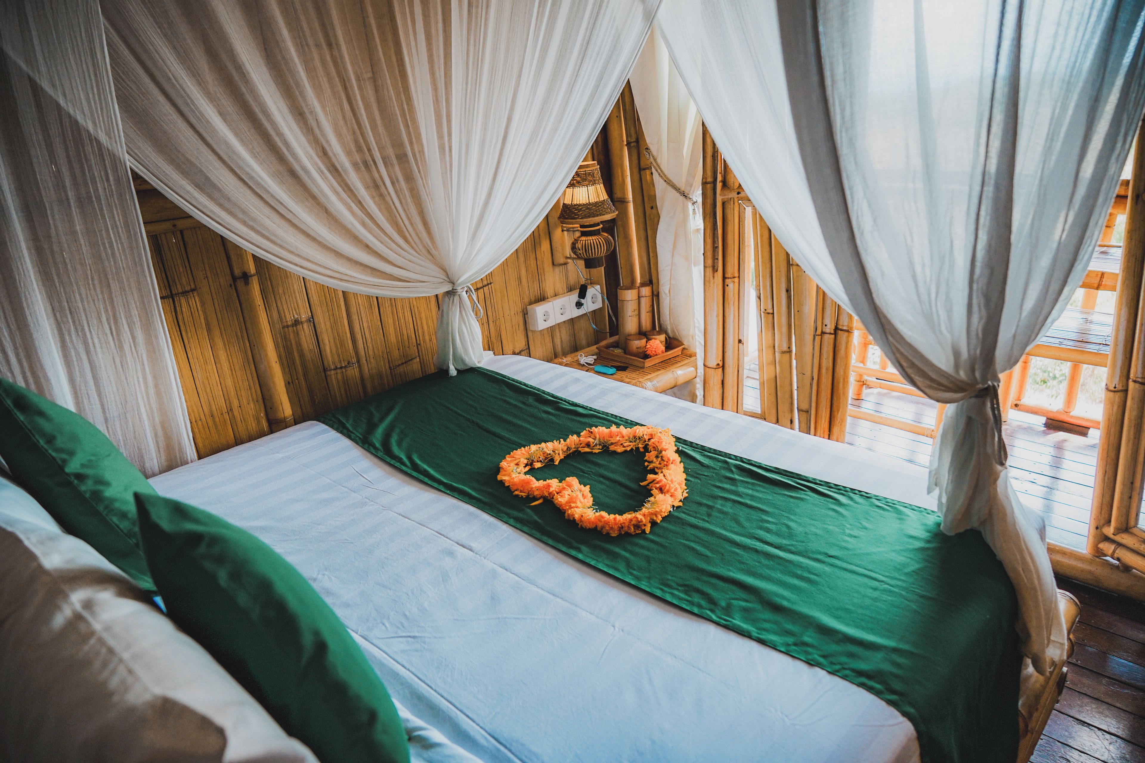 A bed with green bedding and a heart-shaped flower arrangement, wooden walls, and a window with curtains.