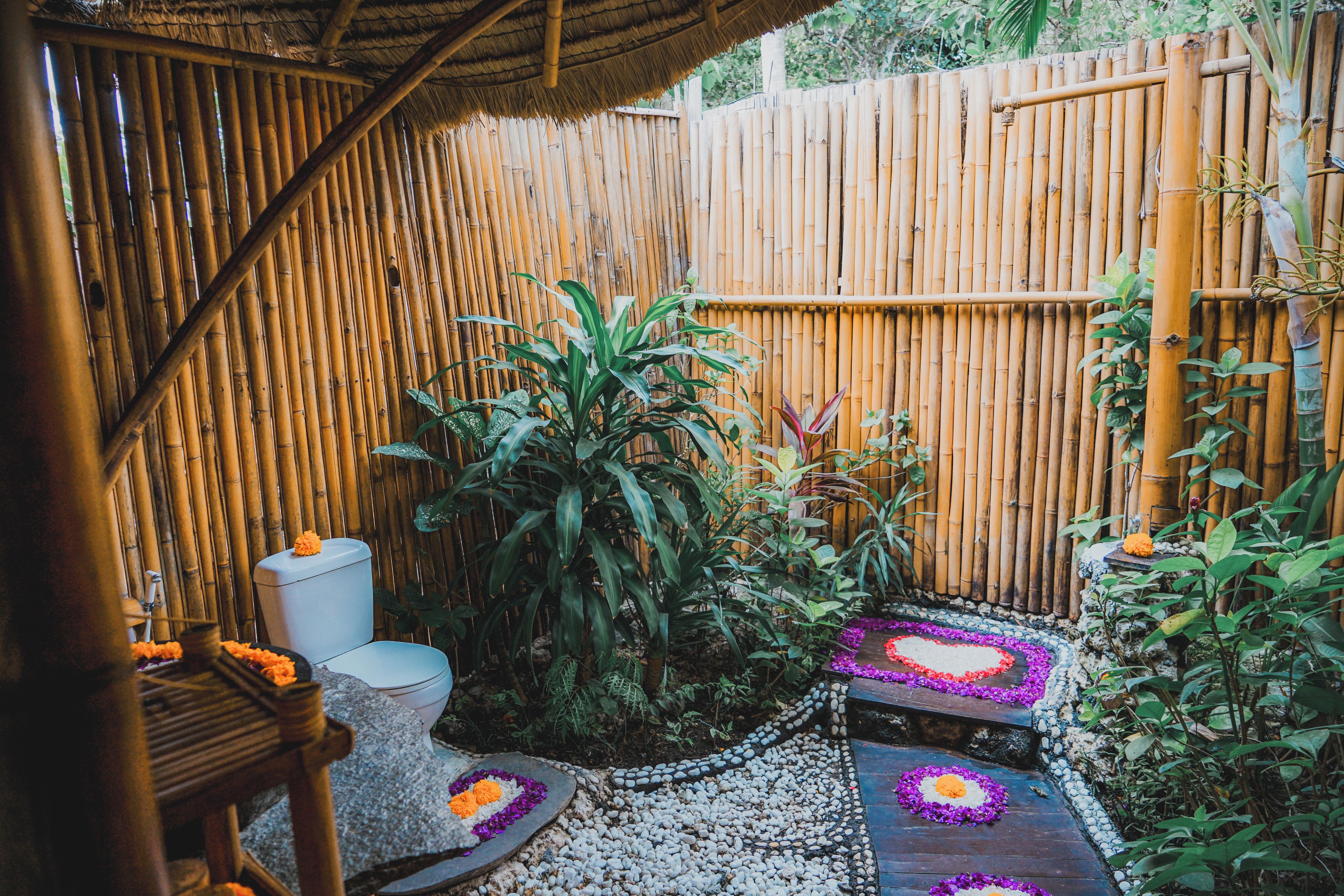 A bamboo fence, a toilet, and a garden area with plants and a stone pathway.