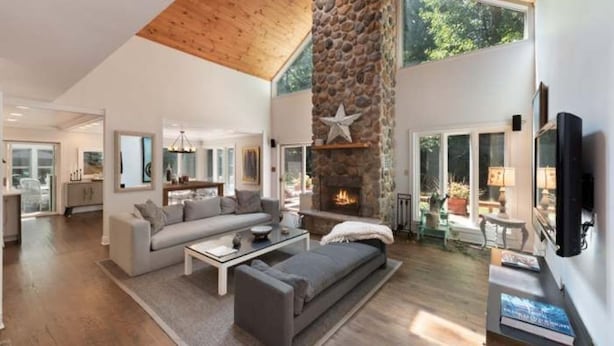 A spacious living area with a stone fireplace, a large sofa, and a television. - Private Cherry Beach Pool House with large heated pool & hot tub!  (Three Oaks)