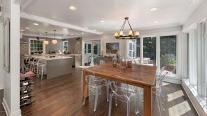A spacious kitchen with a large island, clear chairs, and a wooden dining table. - Private Cherry Beach Pool House with large heated pool & hot tub!  (Three Oaks)