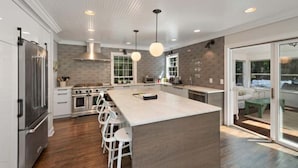 A modern kitchen with a central island, bar stools, stainless steel appliances, and pendant lighting. - Private Cherry Beach Pool House with large heated pool & hot tub!  (Three Oaks)