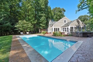 A swimming pool with a stone border, surrounded by a grassy lawn and trees.