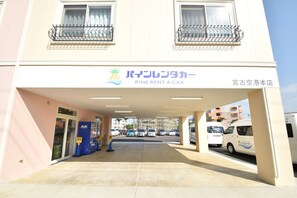 A building with a sign reading "Pine Rent a Car" and a parking area with several cars. - Pine Hills Hotel Miyakojima (Miyakojima)