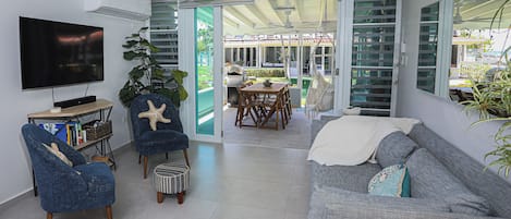 A living room with a TV, blue armchairs, a grey sofa, and a dining area with a table and chairs.