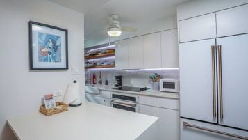 A modern kitchen with white cabinets, a stainless steel refrigerator, and a ceiling fan.