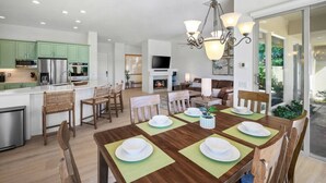 Une cuisine moderne avec des meubles verts, des appareils en acier inoxydable et un coin repas doté d’une table en bois, mise pour quatre personnes.