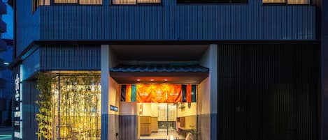 A modern building with a large entrance, a covered outdoor seating area, and a visible sign with Japanese characters.