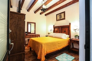 A bedroom with a wooden bed, a nightstand, a dresser, and a mirror. - El Mesón del Quijote (San Miguel de Allende)