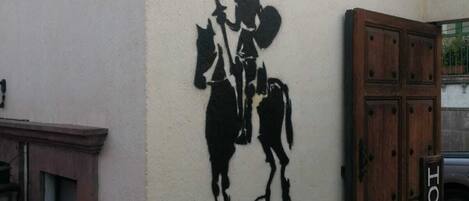 Un edificio con un mural de un jinete a caballo, una puerta de madera con la leyenda 'HOTEL' y un muro de piedra.