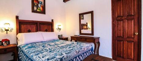 A bedroom with a wooden bed, a nightstand with a lamp, a dresser, a mirror, and a wooden door.