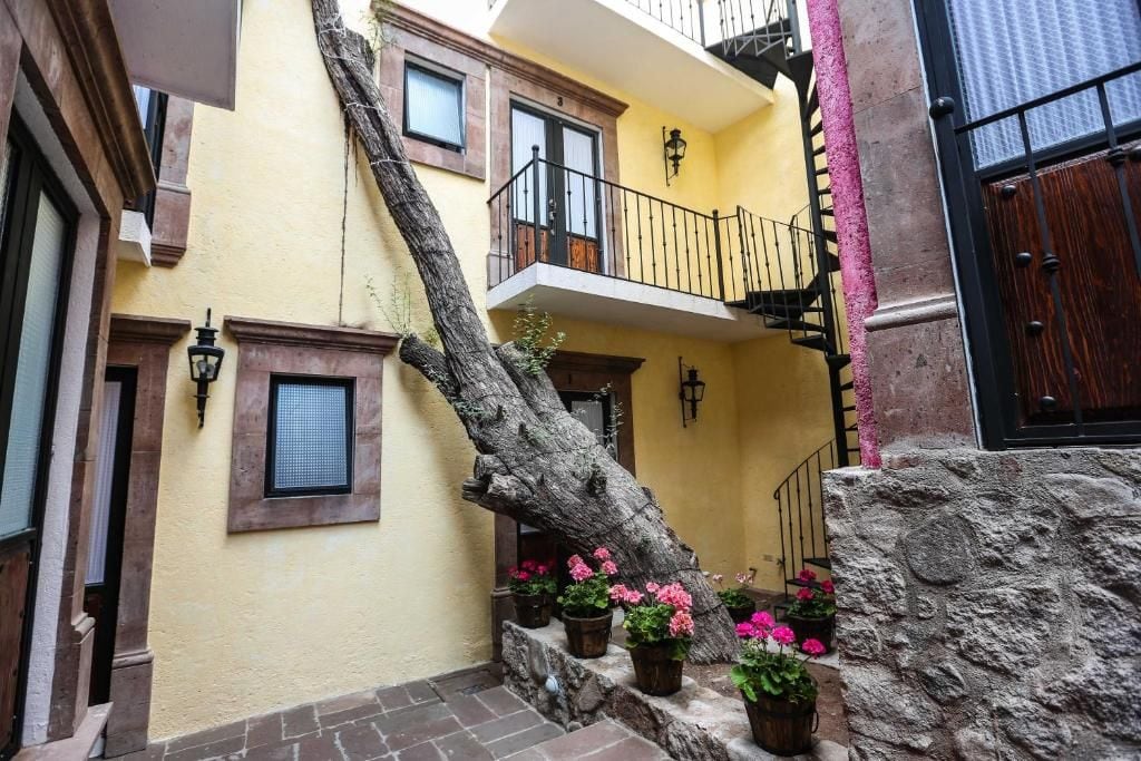 Un edificio amarillo con balcón, plantas en macetas y una pared de piedra.