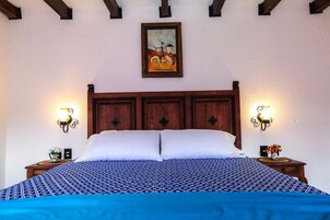 Un dormitorio con una cama grande, cabecera de madera, dos lámparas fijadas a la pared y un cuadro sobre la cama.