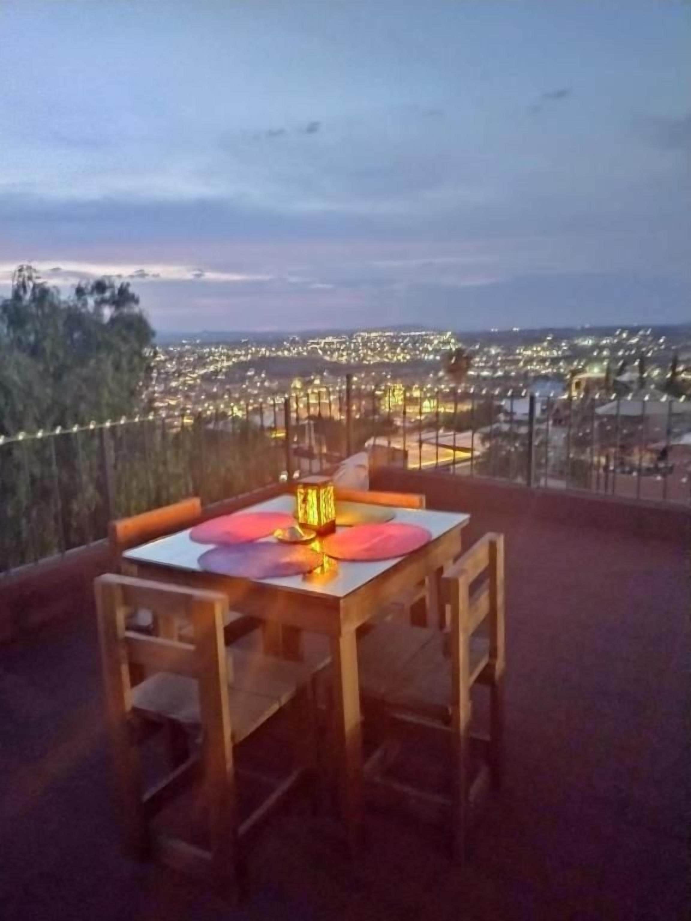 Una mesa con sillas en una terraza con vistas a un paisaje urbano al atardecer.
