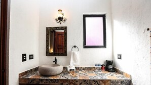 Un baño con un lavamanos grande y redondo, un espejo, una luz empotrada en la pared y una ventana con marco negro.