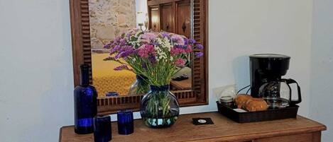 A wooden desk with a mirror, a vase of flowers, a coffee maker, and a tray with pastries.
