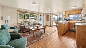 A spacious living room with a sofa, a coffee table, and a rug. There is a kitchen area with wooden cabinets and a countertop. - Outdoor adventures all around this comfy home with stunning views prime location (Hamilton)