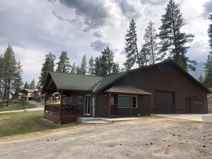 Surrounded by tall pine trees, this rustic lodge features a large garage door and a covered porch area.