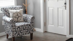 Una habitación con techo de madera, una puerta blanca, un sillón estampado y un círculo salvavidas colgado en la pared.
