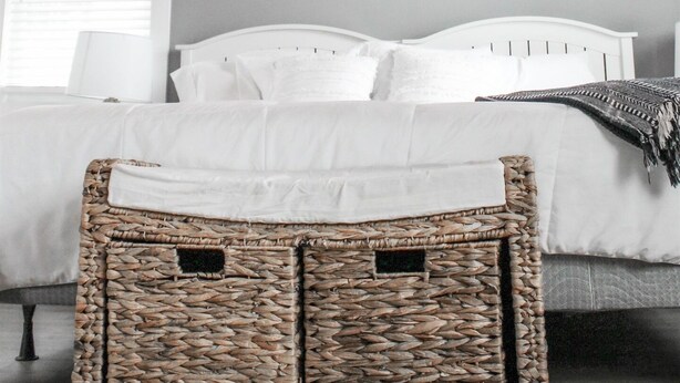 Un dormitorio con techo inclinado, una cama, un equipo de aire acondicionado blanco y un baúl de mimbre.