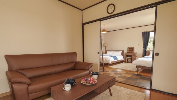 A cozy room with a brown leather sofa, a wooden coffee table with cups and a plate, and a checkered floor. - Maru House (Uruma)