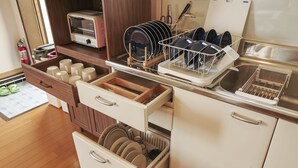 A kitchen with wooden cabinets, a toaster, and a dish rack with plates and bowls. - Maru House (Uruma)