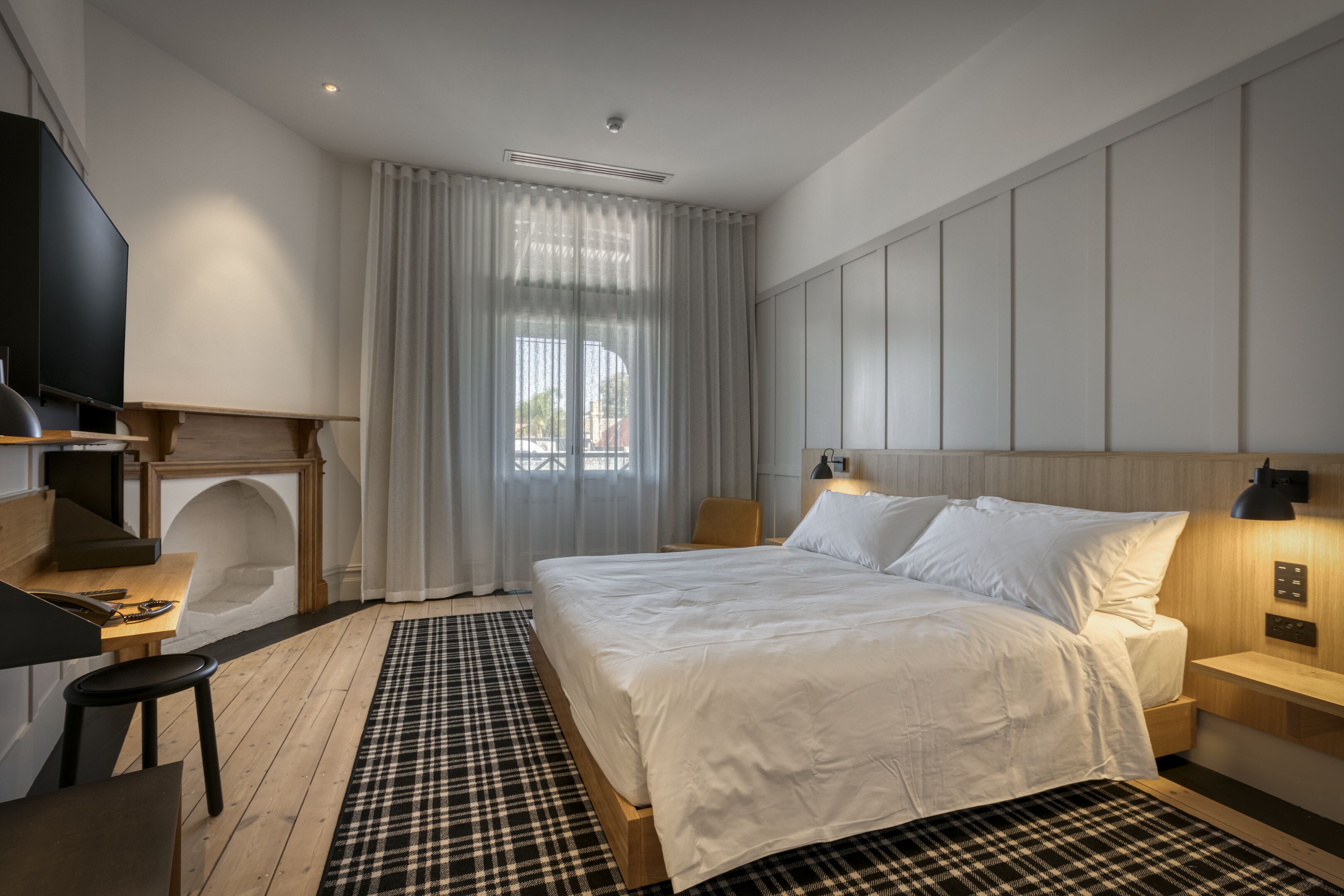 A modern hotel room with a large bed, a desk with a chair, a TV, and a fireplace.