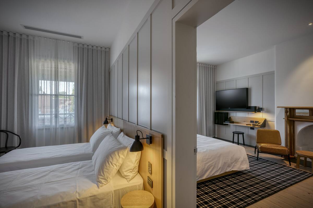 Une chambre d’hôtel moderne équipée de deux lits, d’une télévision, d’un petit bureau et d’une cheminée.