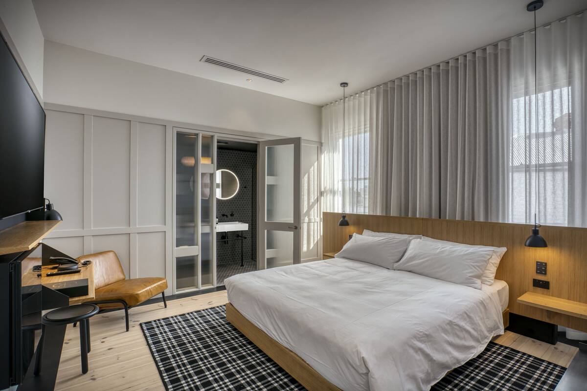 Une chambre d’hôtel moderne dotée d’un grand lit, d’un bureau avec une chaise, d’une télévision et d’une salle de bain avec une porte en verre.