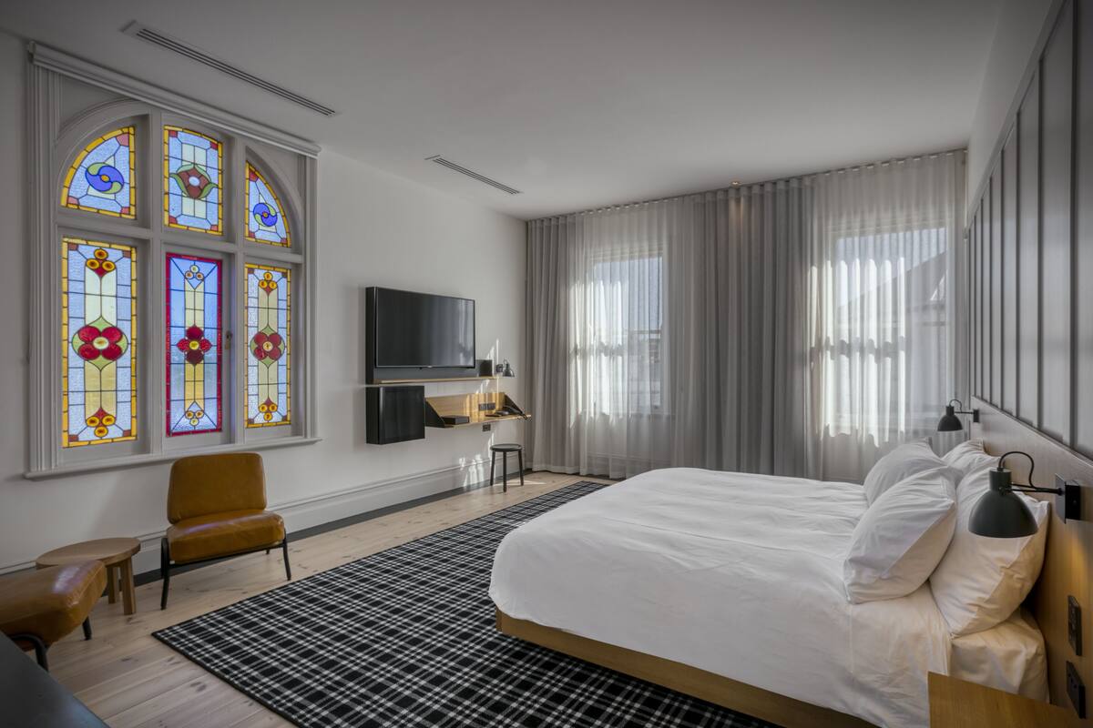Une chambre d’hôtel moderne, dotée d’un grand lit, d’une télévision, d’un bureau, d’une chaise et d’une fenêtre ornée de vitraux.