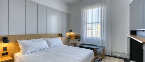 Ett modernt hotellrum med en stor säng, ett skrivbord, en stol och en TV.