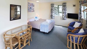 Een slaapkamer met een bed, een televisie, een bureau en rieten meubels.