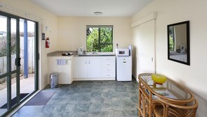 Een kleine keuken met witte kastjes, een magnetron en een raam.
