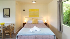Een hotelkamer met een bed, nachtlampjes, een kleintje tafeltje met stoelen, een spiegel en een raam met gordijnen.