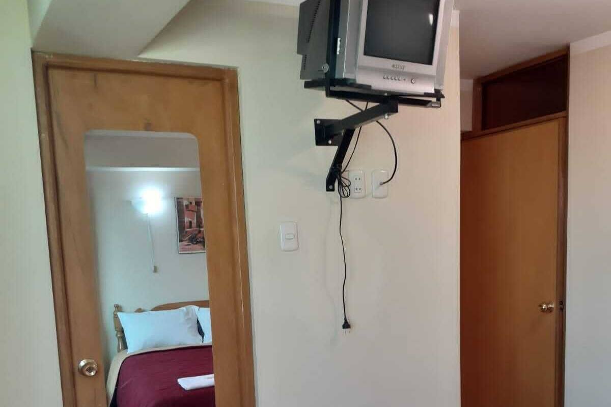 Een slaapkamer met een bed, een aan de muur bevestigde televisie, een houten deur en een rode sprei.