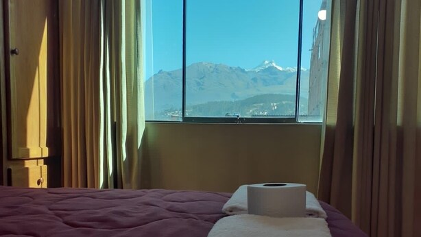 A hotel room with a bed, a window with a mountain view, and a rolled-up towel on the bed. - Lhotse Hostel B&B Huaraz (Huaraz)