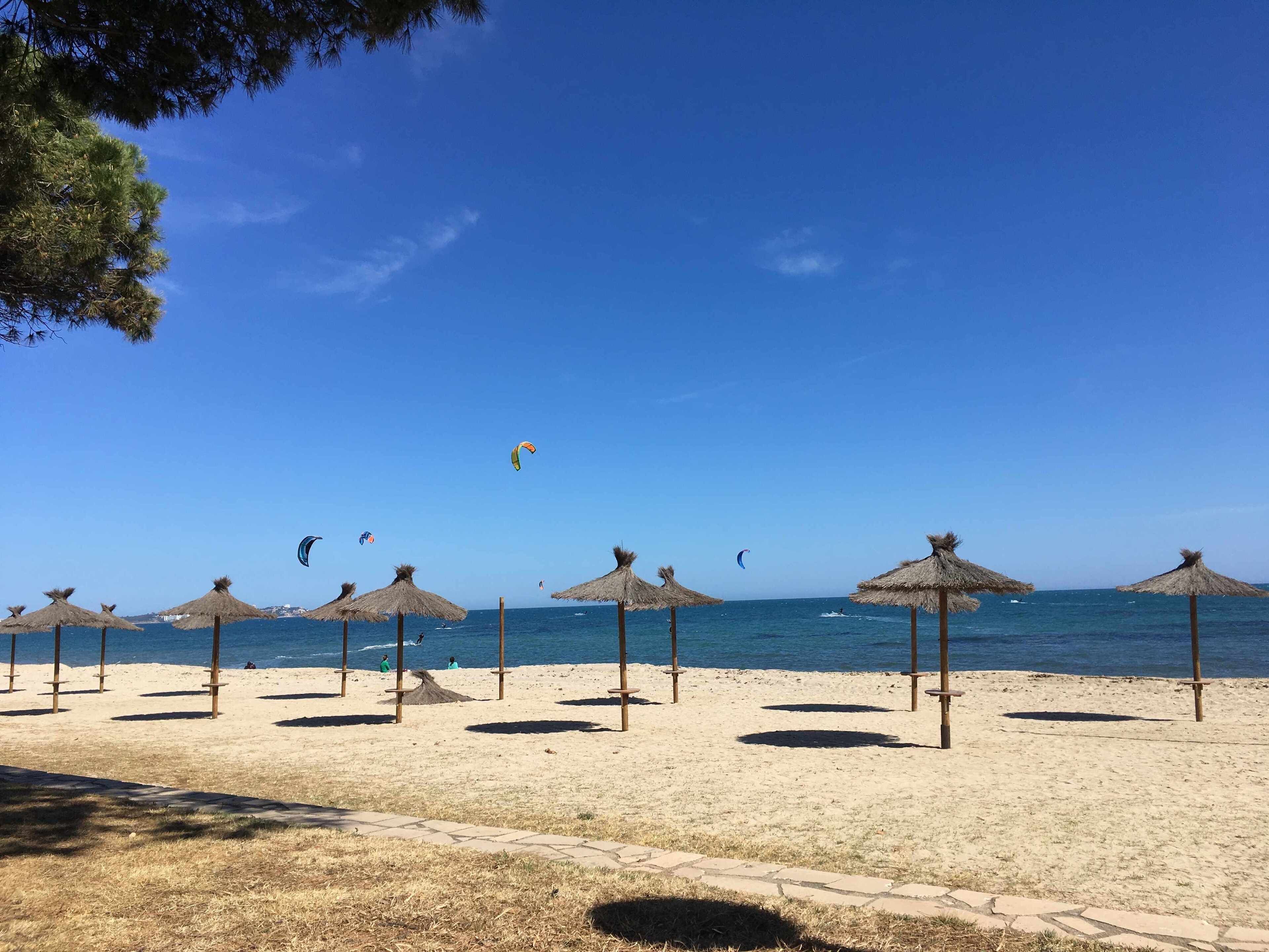 A beach with thatched umbrellas and a clear blue sky.
