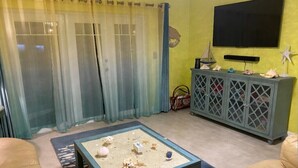 Un salon avec une table basse en verre, des canapés en cuir, un téléviseur et un meuble contenant des objets décoratifs.